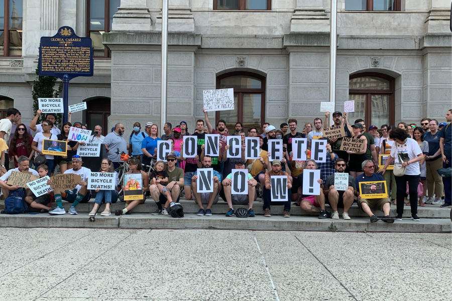 Group of people outside Philadelphia's City Hall holding signs that read "Concrete Now" at a rally for safer bike lanes.
