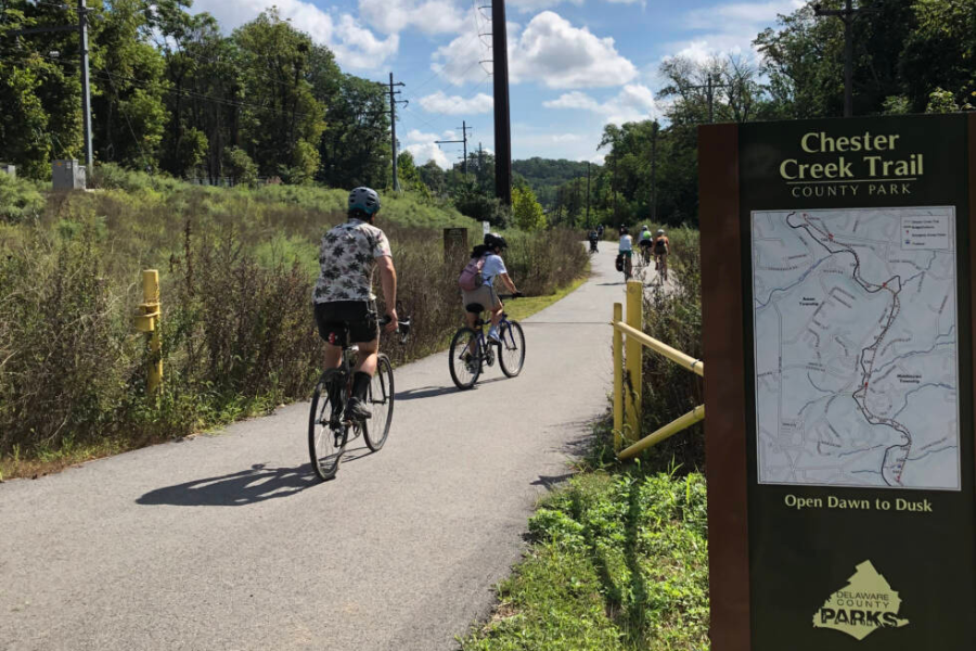 People riding bikes along the Chester Creek Trail next to a trail marker with a map that reads "Chester Creek Trail County Park."