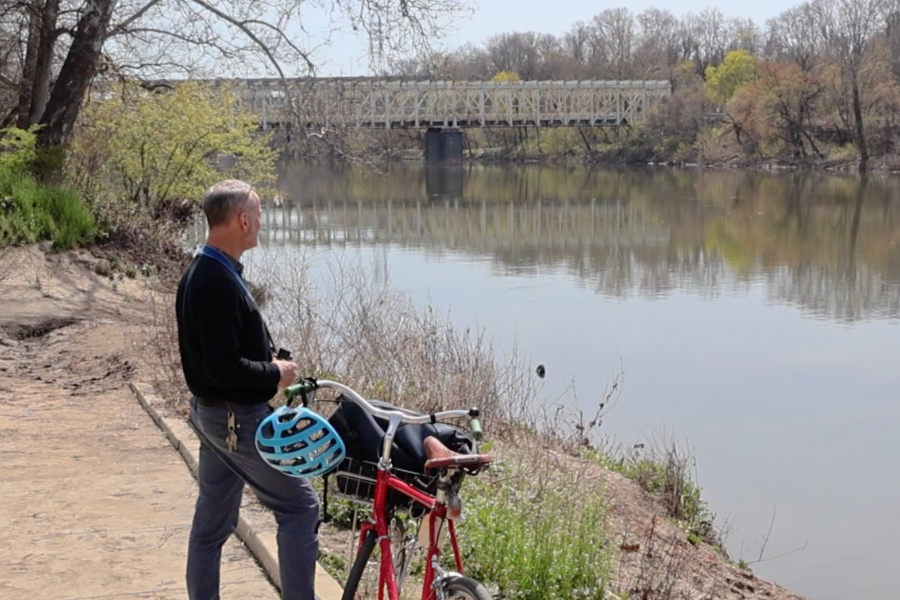 Man standing on landing next to a bike with a blue helmet looking into the river