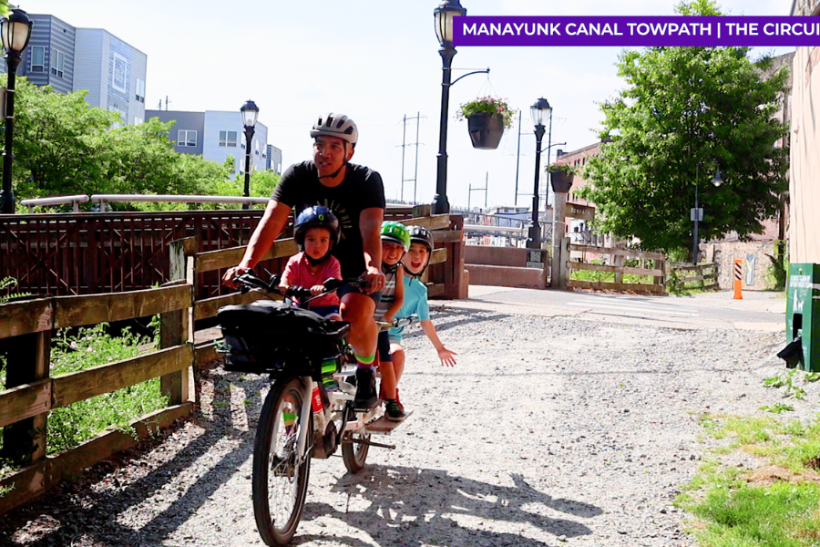 Man riding a cargo bike with three children. One child is on a saddle in the front and two are in a cargo seat in the back.