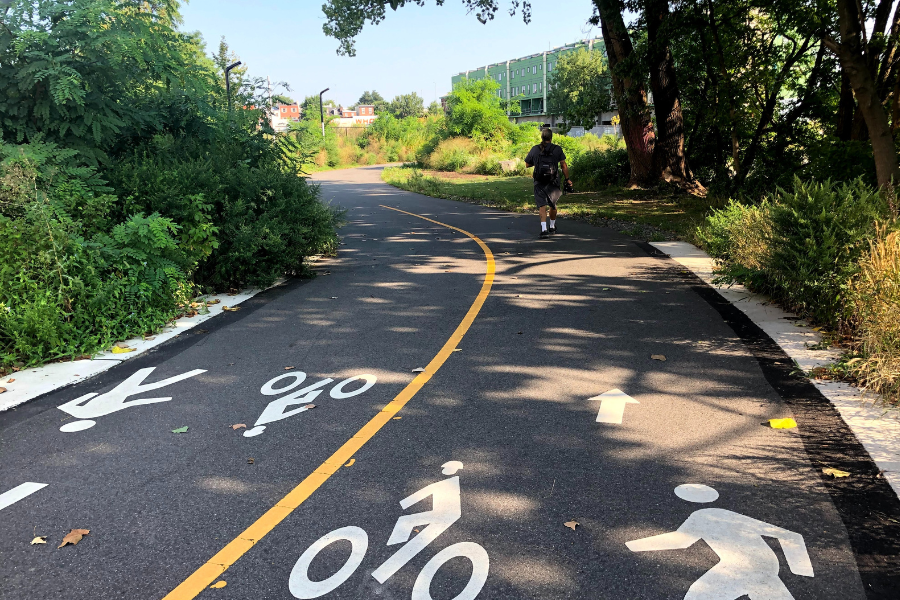 one person walking on a paved trail that has a yellow line splitting the middle of the trail with pedestrian and cyclist icons on the trail ground