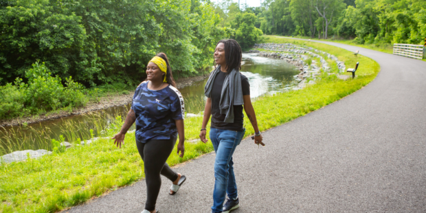 A young man and women wearing casual clothes walking on the paved Chester Creek Trail.
