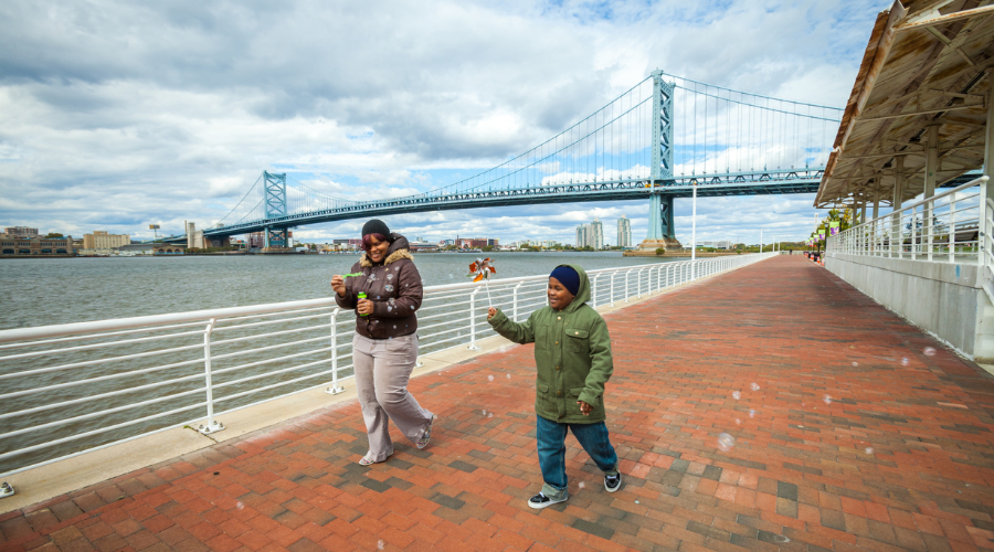 two people in winter jackets blowing bubbles while walking along the Ulysses Wiggins Waterfront Promenade
