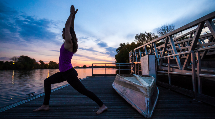 a woman standing in a yoga pose on a boat launch during the sunset