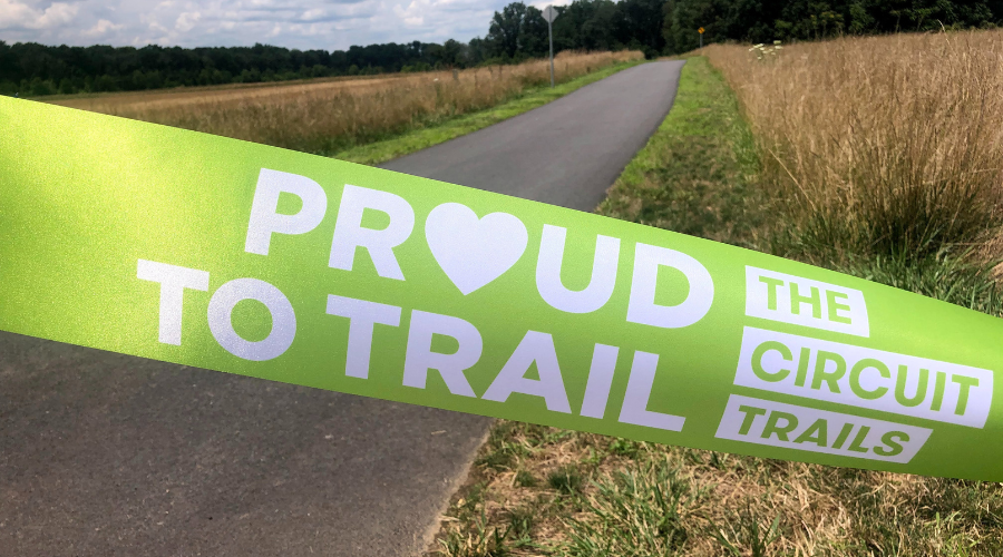 Green proud to trail ribbon across a newly paved trail before a ribbon cutting ceremony